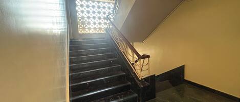 A staircase with a wooden handrail and black steps leading to a landing.