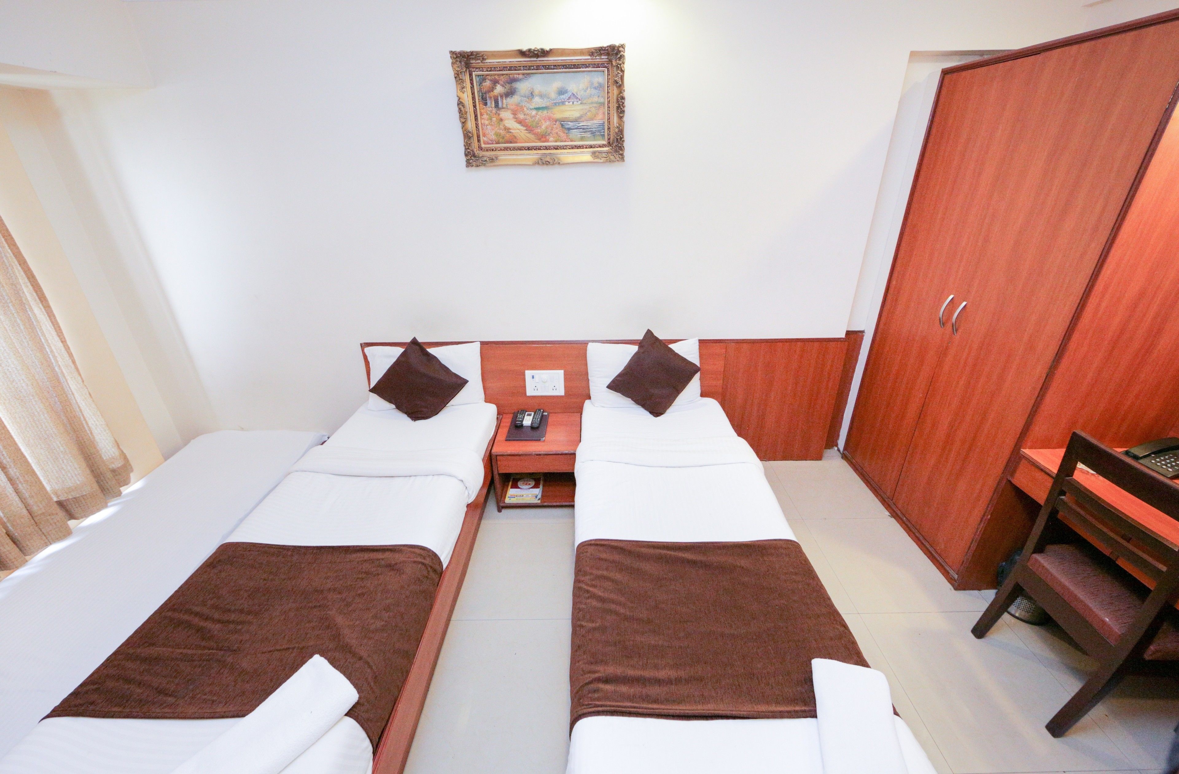 A twin room with two beds, a wooden wardrobe, a small table, and a chair.