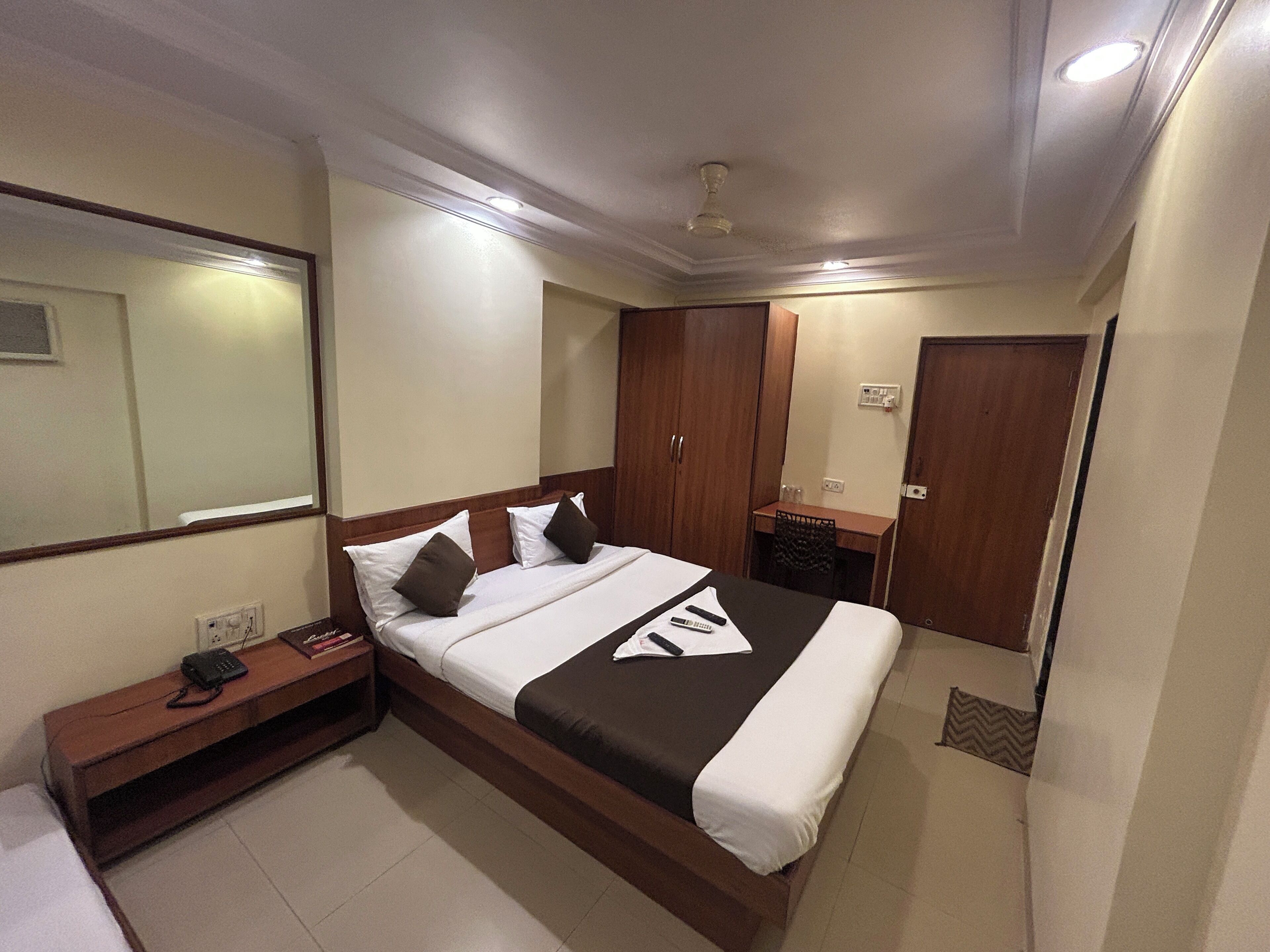 Ein Hotelzimmer mit Bett, Nachttisch, Schreibtisch, Kleiderschrank und Spiegel.