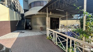 Un espacio exterior techado con una escalera que sube a un nivel superior, una motocicleta estacionada y una silla cerca de la entrada.