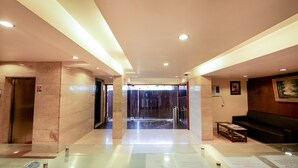 Un vestíbulo amplio con un ascensor de cristal, un mostrador de recepción y una zona de estar.