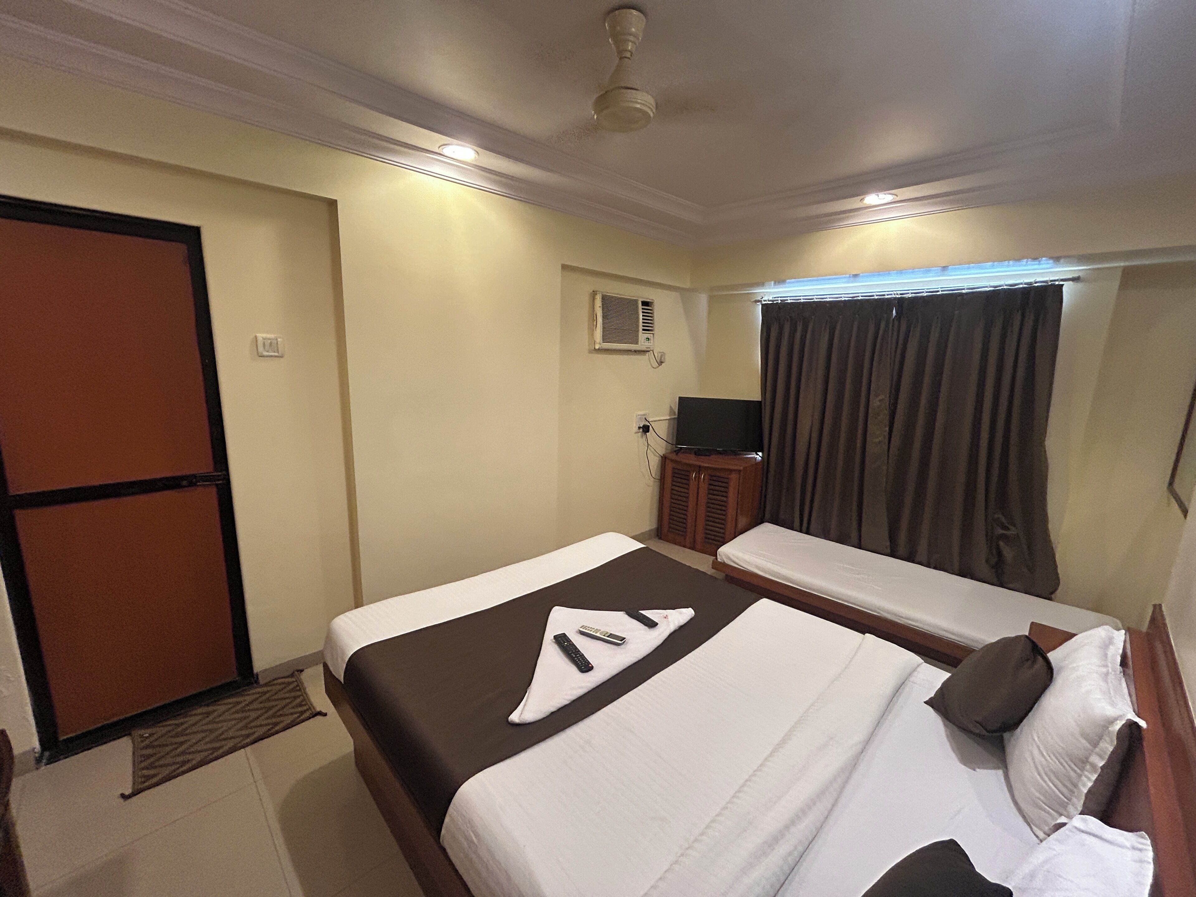 A hotel room with a bed, a desk, a TV, and a window with curtains.
