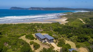 A coastal property with a modern two-story building, surrounded by dense greenery and a beach.