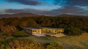 A modern house with glass walls, a flat roof, and a deck.