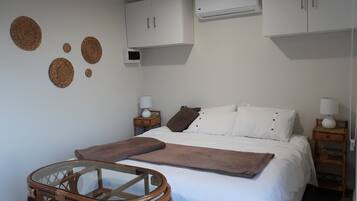 Un dormitorio con una cama, dos mesitas de noche, una silla de madera pequeña y un aire acondicionado de pared.