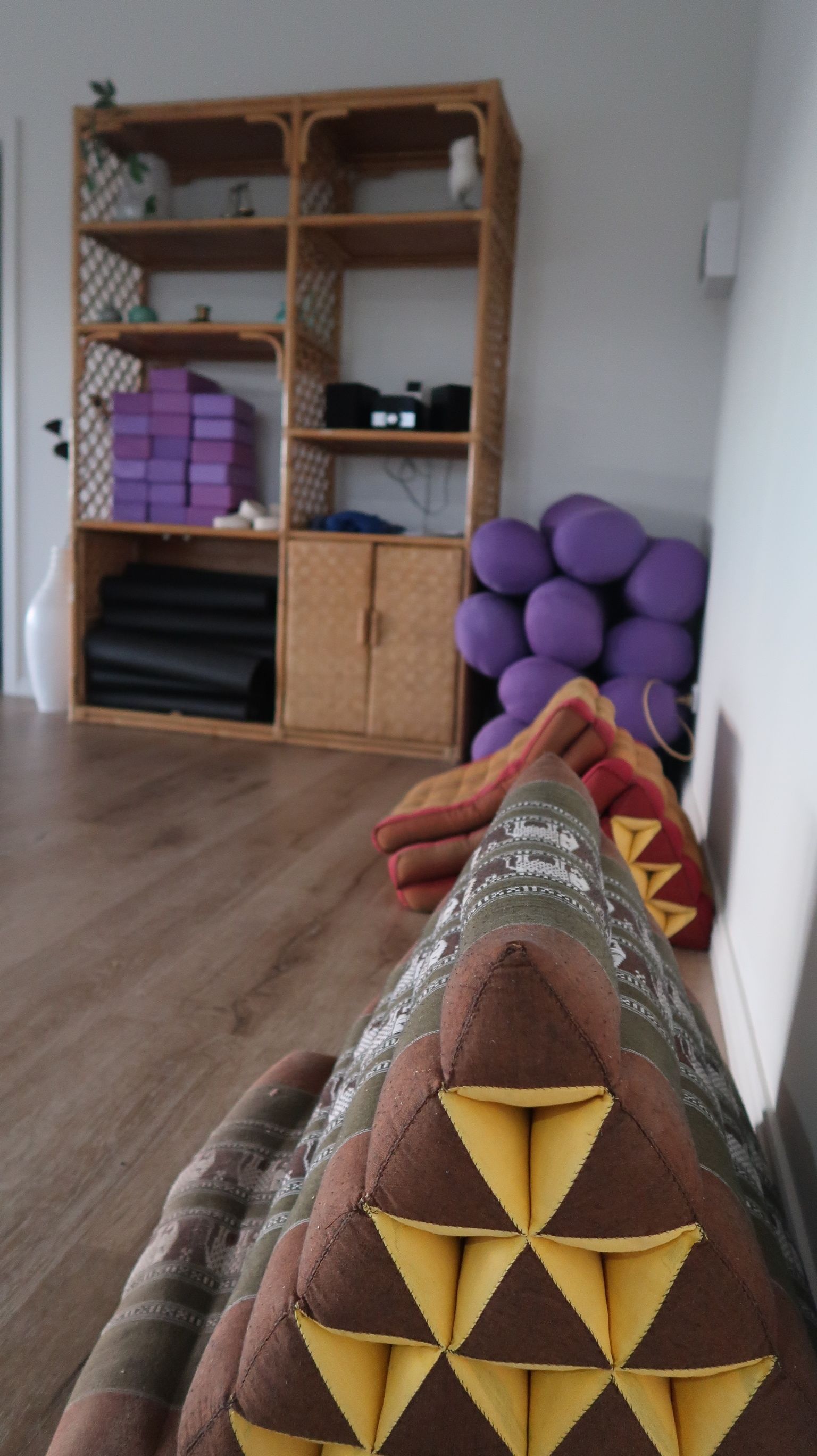 A room with a wooden floor, a wicker shelf with various items, and a pair of legs with patterned leggings.