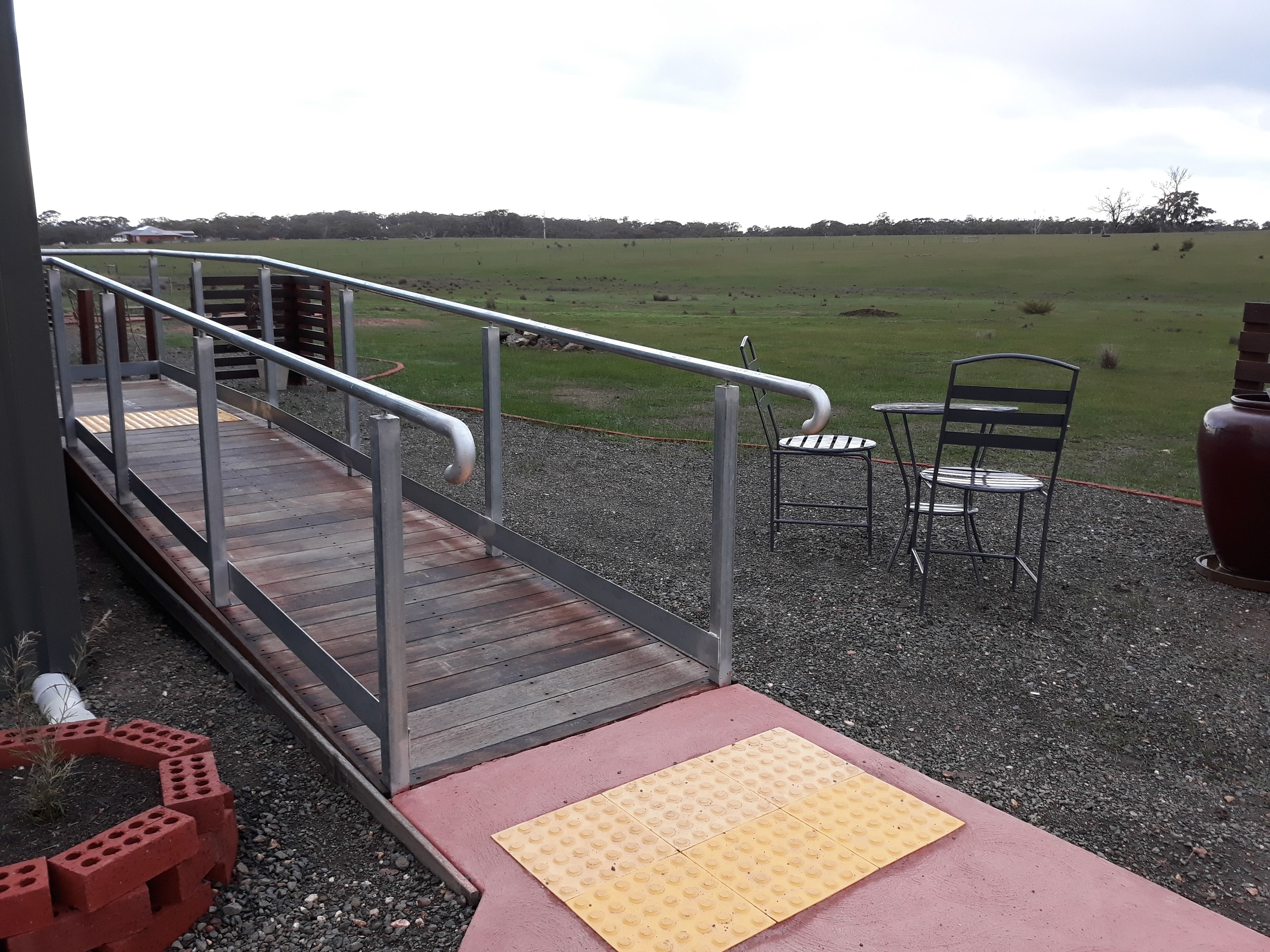A wooden deck with a metal railing, a tactile paving path, and outdoor seating.