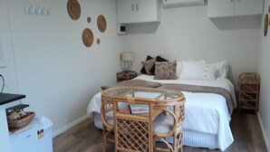Ein Schlafzimmer mit einem Bett, Nachttischen, einem Glastisch, Korbstühlen und einem weißen Kleiderschrank.