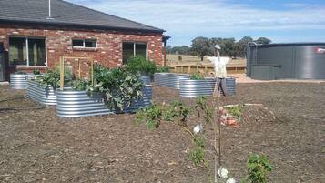 A brick building with a metal roof, surrounded by raised garden beds and a field in the background.