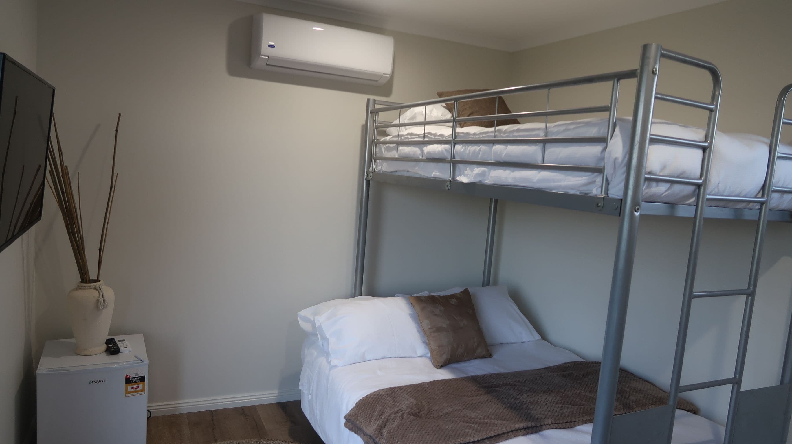 A bunk bed room with a white wall, a small bedside table with a lamp, and an air conditioning unit above the bed.