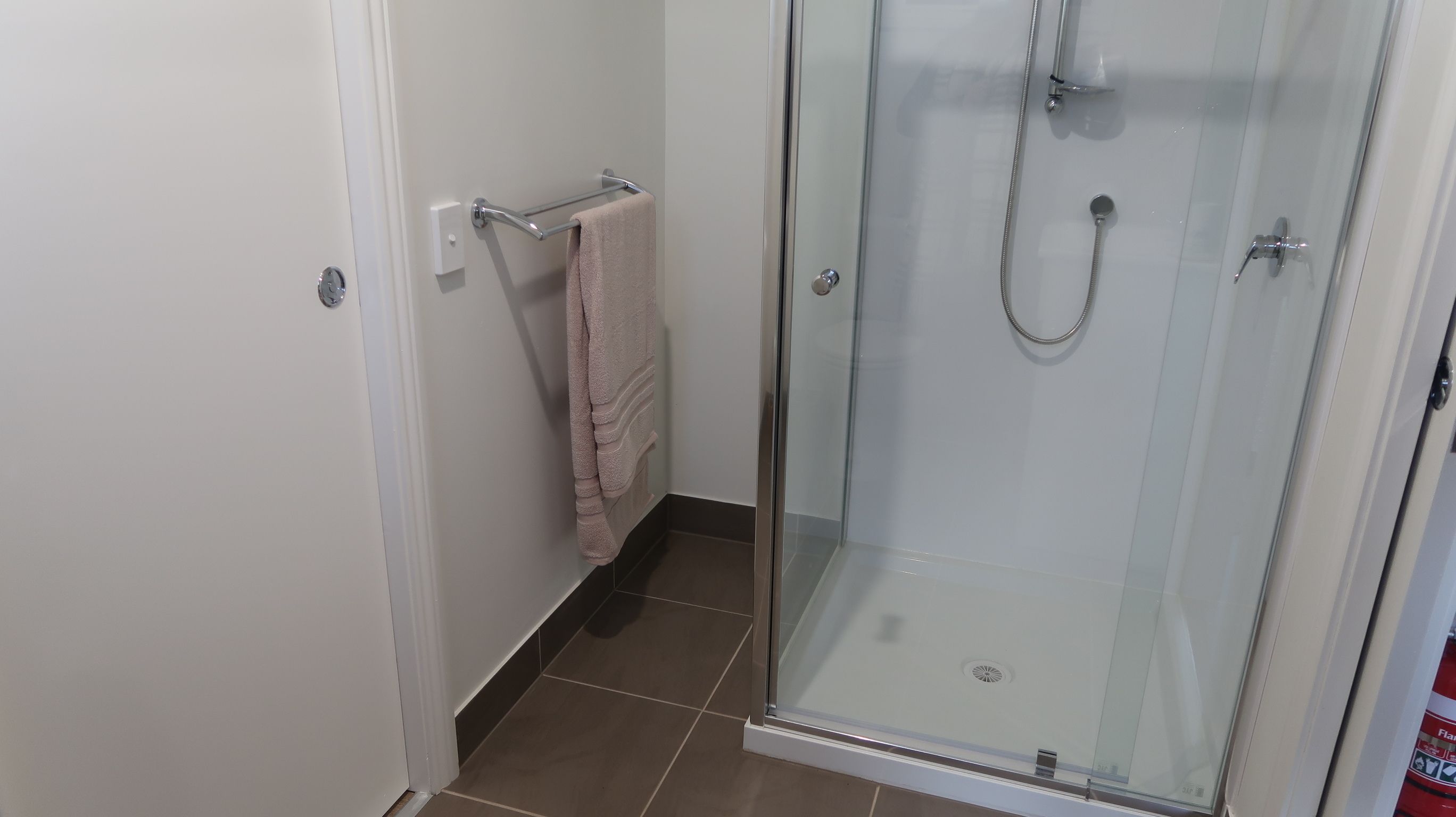 Ducha con cerramiento de vidrio, cabezal de ducha de mano y toallero con una toalla.