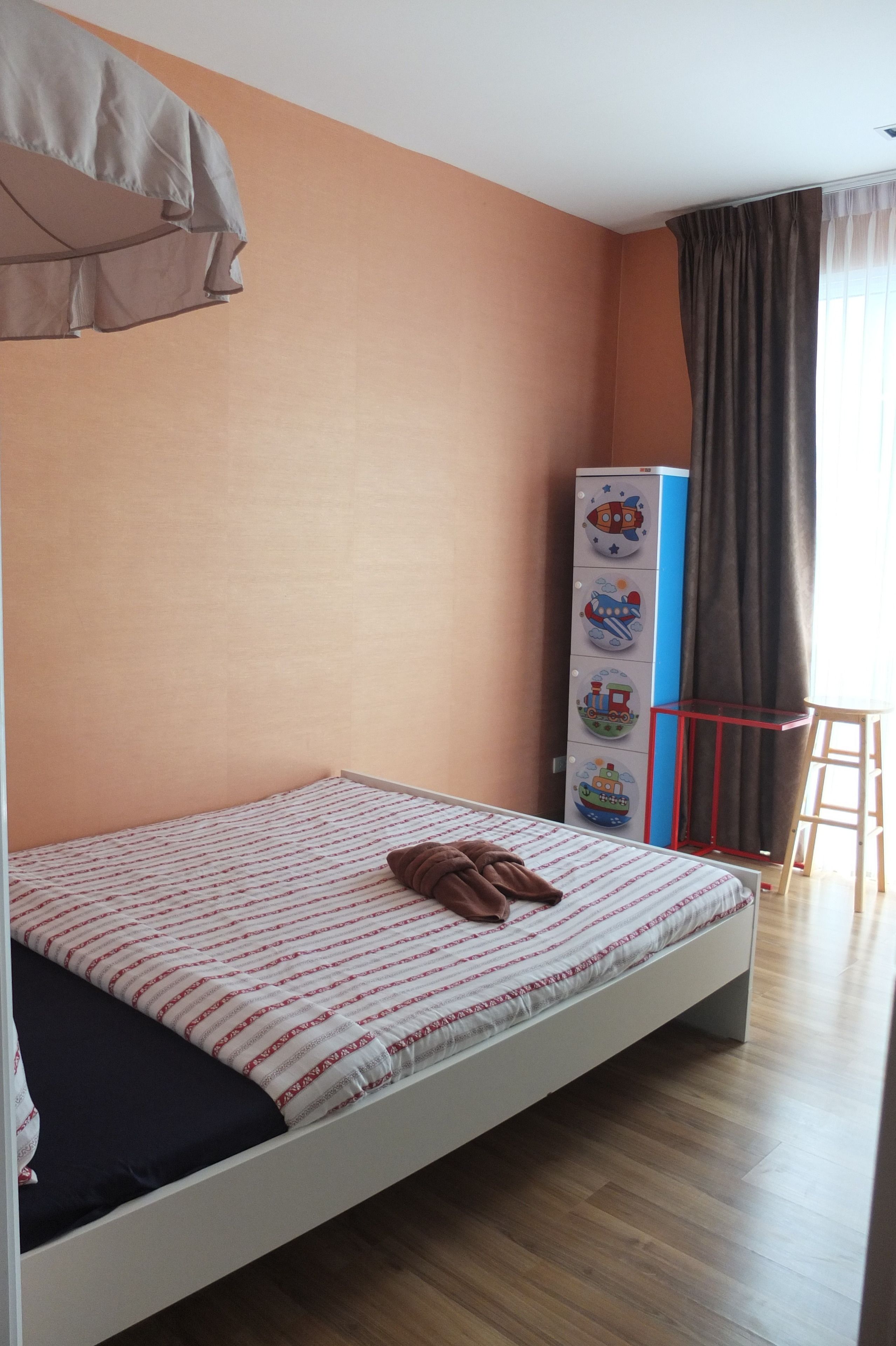 Ein Schlafzimmer mit einem Bett, einem Schrank mit Kinderzeichnungen, einem Vorhang und einem kleinen Tisch.