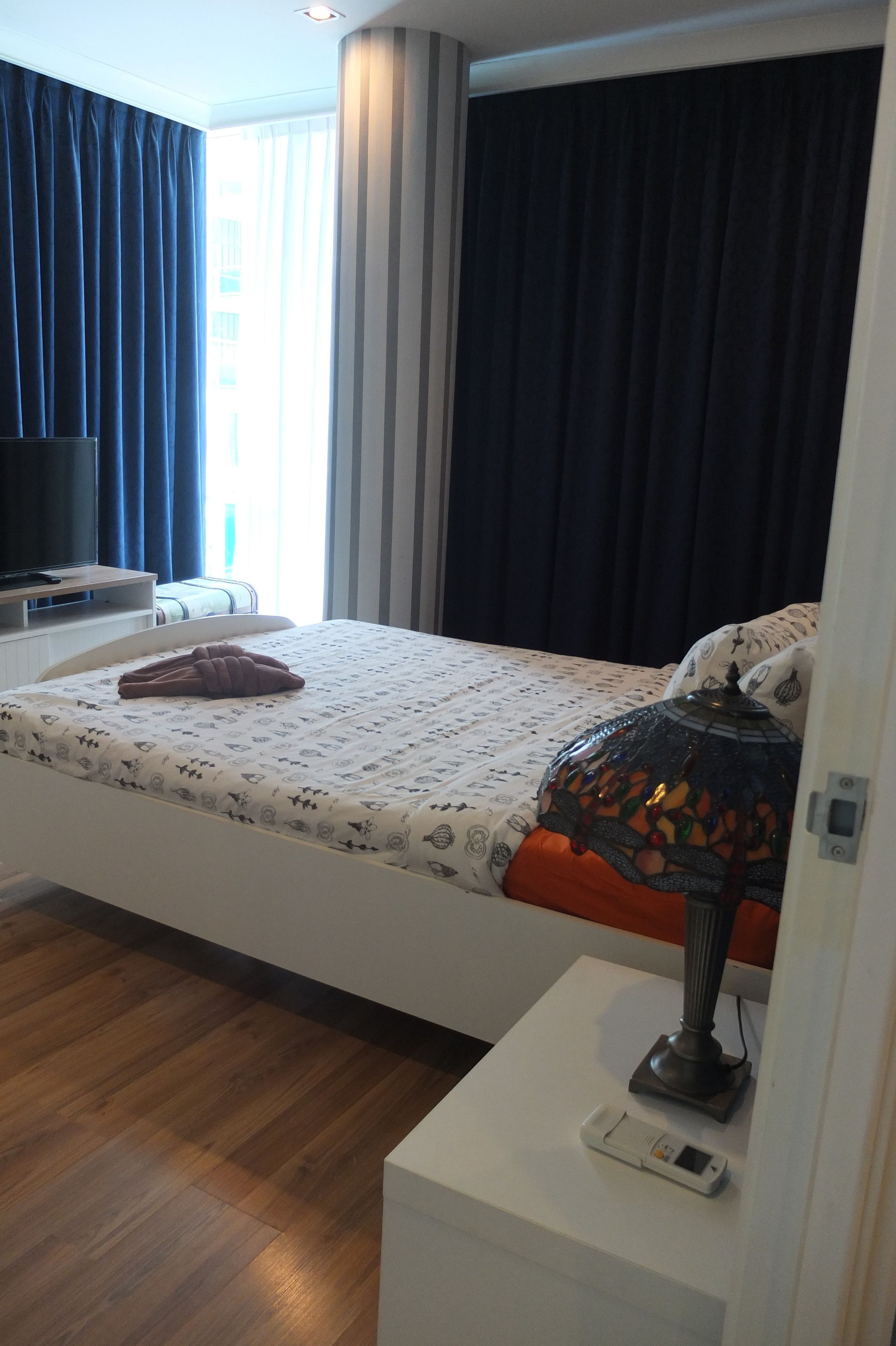 Habitación de hotel con cama, televisión, lámpara y mesita de noche.