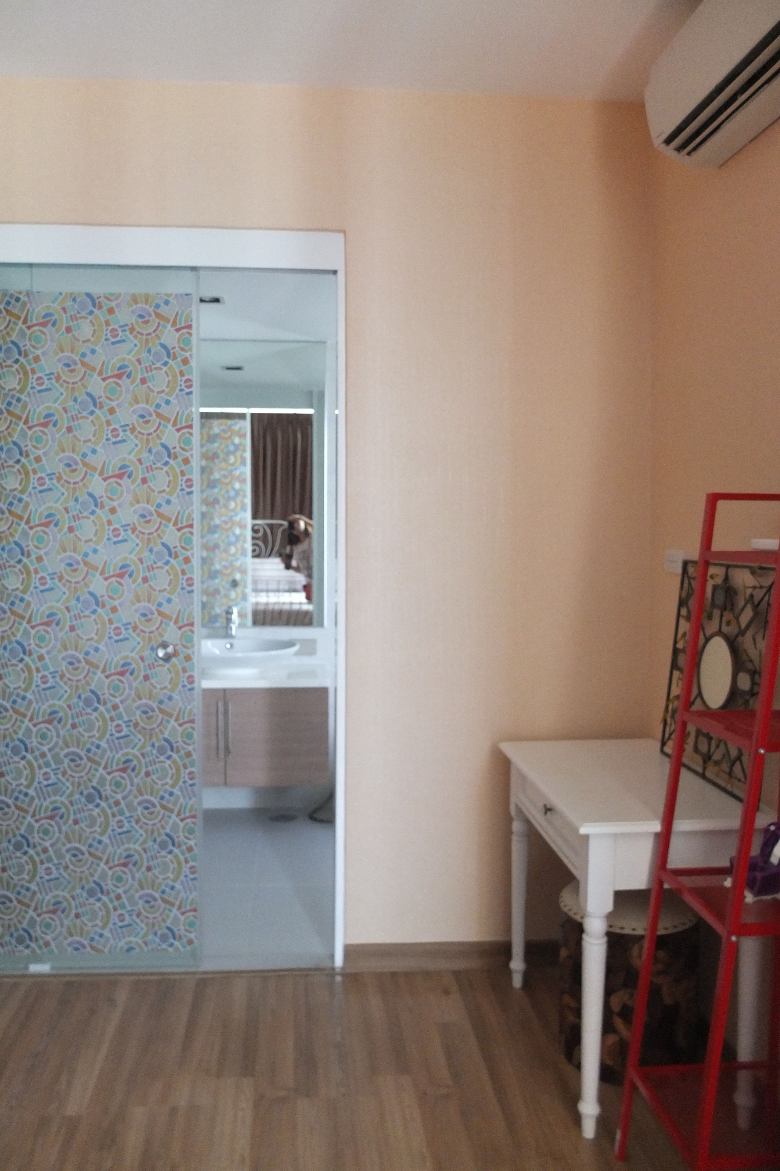 A room with a wooden floor, a white desk, a red ladder, and a patterned door.