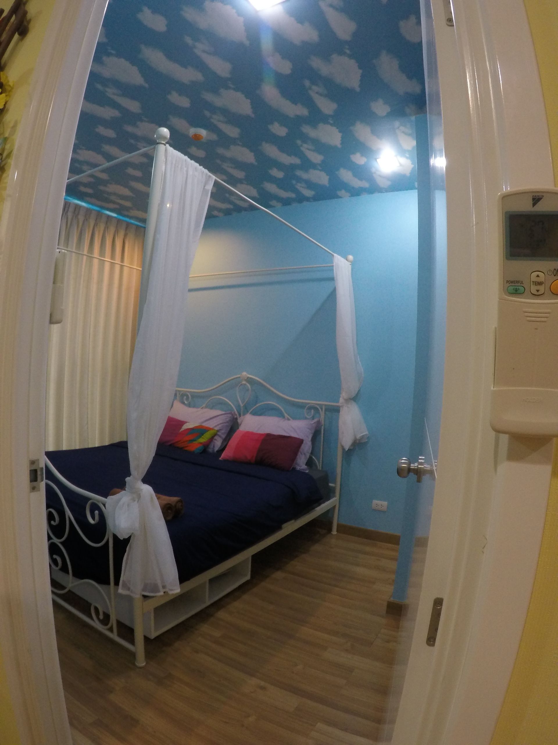 A bedroom with a canopy bed, a ceiling with a cloud pattern, and a thermostat on the wall.