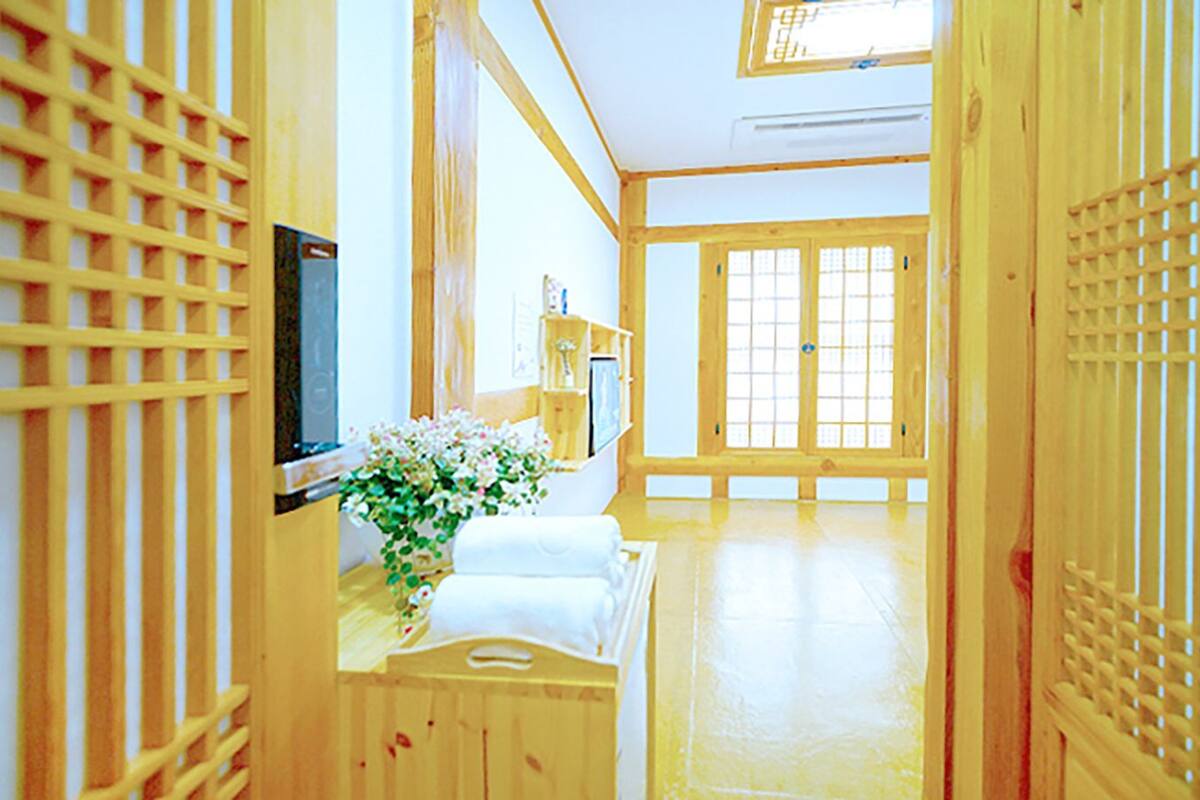 A traditional Japanese room with tatami flooring, a low wooden desk, a bed with white bedding, and sliding doors.