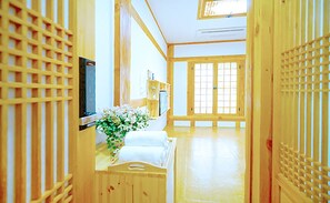 A traditional Japanese room with tatami flooring, a low wooden desk, a bed with white bedding, and sliding doors.