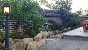 A courtyard with a traditional brick wall, a stone pathway, and a wooden bench. - Lee Ga Hanok (Jeonju)