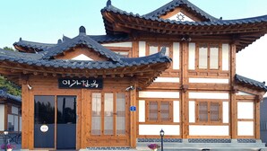A traditional wooden building with a sign in Korean, a wooden door, and a small entrance area with a flower pot. - Lee Ga Hanok (Jeonju)