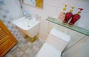 A bathroom with a white sink, a glass shelf with toiletries, and a toilet.