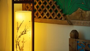 Une pièce dotée d’un mur en treillis de bois traditionnel, d’une lampe au motif floral et d’une tête de lit en bois ornée d’une sphère décorative.