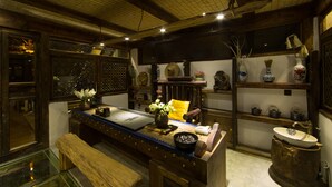 Une pièce à l’ancienne, avec un bureau en bois, un banc, une grande fenêtre et un lavabo rustique.