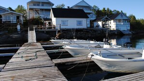 A wooden dock with several boats moored at a marina, surrounded by houses with a stone foundation and a clear blue sky. - Furoy Hotel Apartments and Boating (Sorreisa)