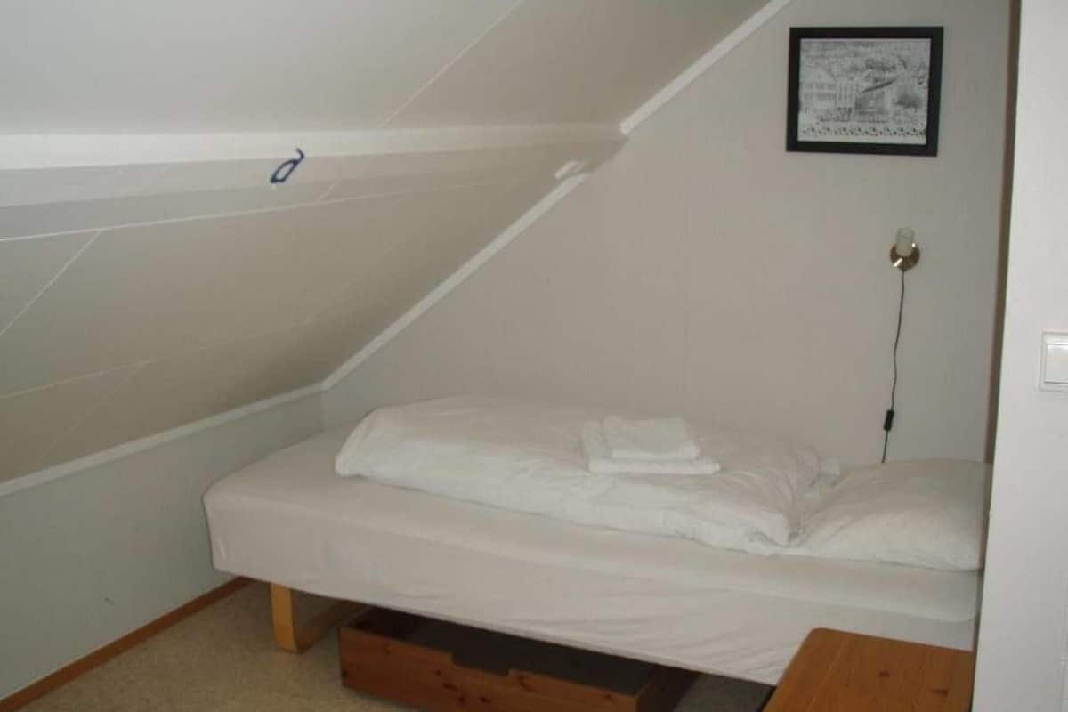 A small, single-bed room with a sloped ceiling and a wooden nightstand.