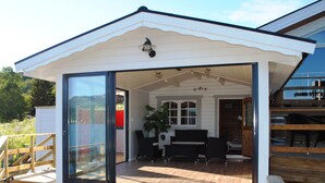 A modern house with a glass door leading to an outdoor patio area with wooden flooring and black furniture. - Furoy Hotel Apartments and Boating (Sorreisa)