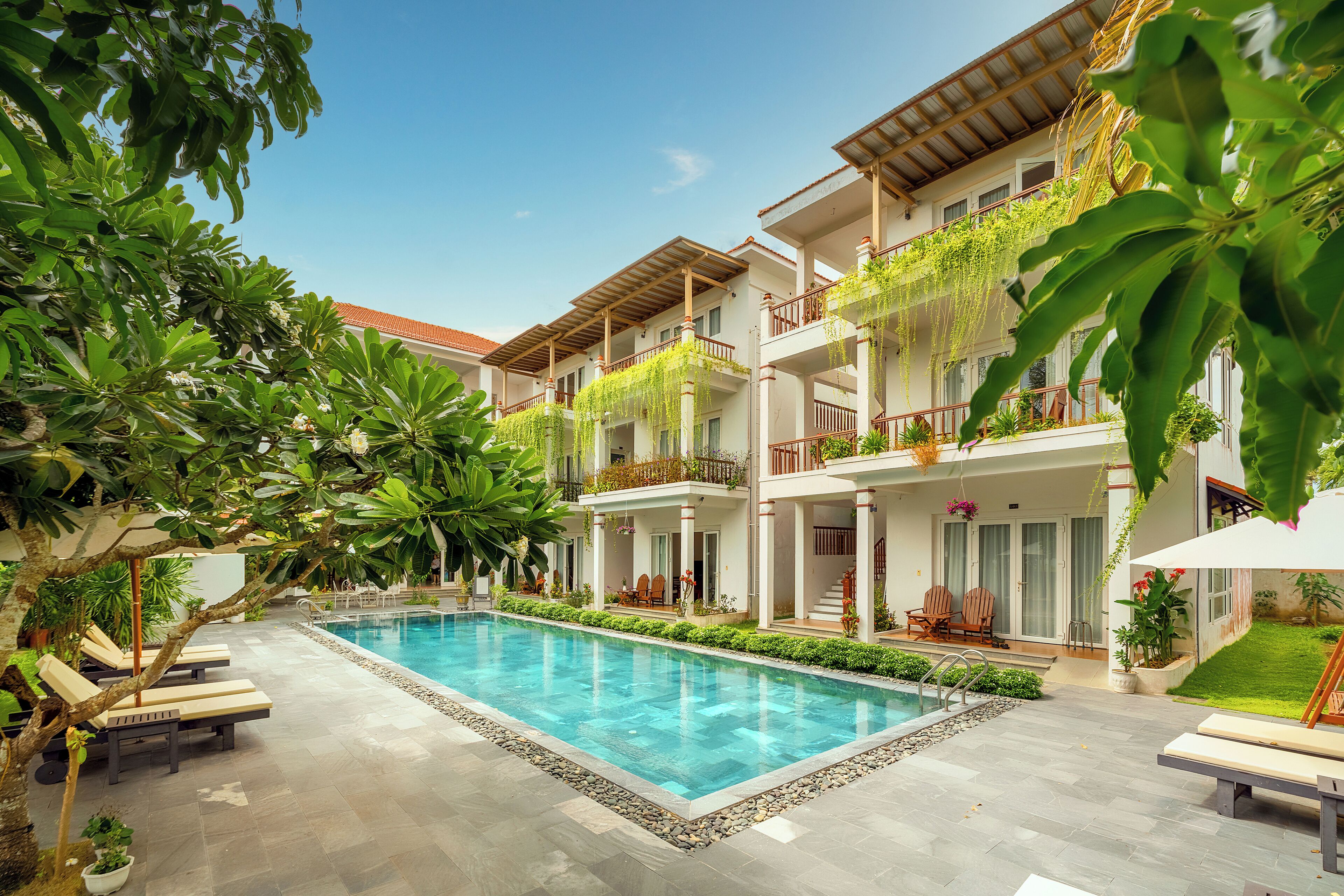 Un hôtel doté d’une piscine, de chaises longues et d’une végétation luxuriante.