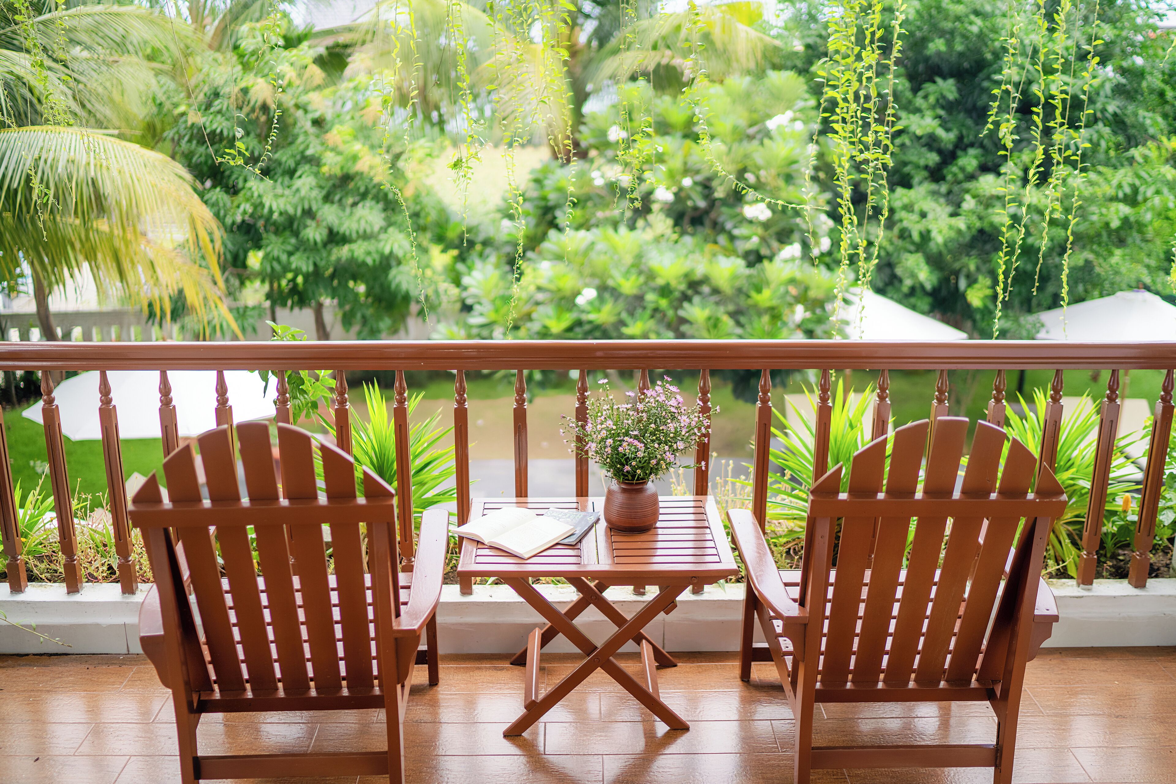 Une terrasse en bois avec deux chaises et une table, un pot de fleurs et une vue sur une végétation luxuriante.