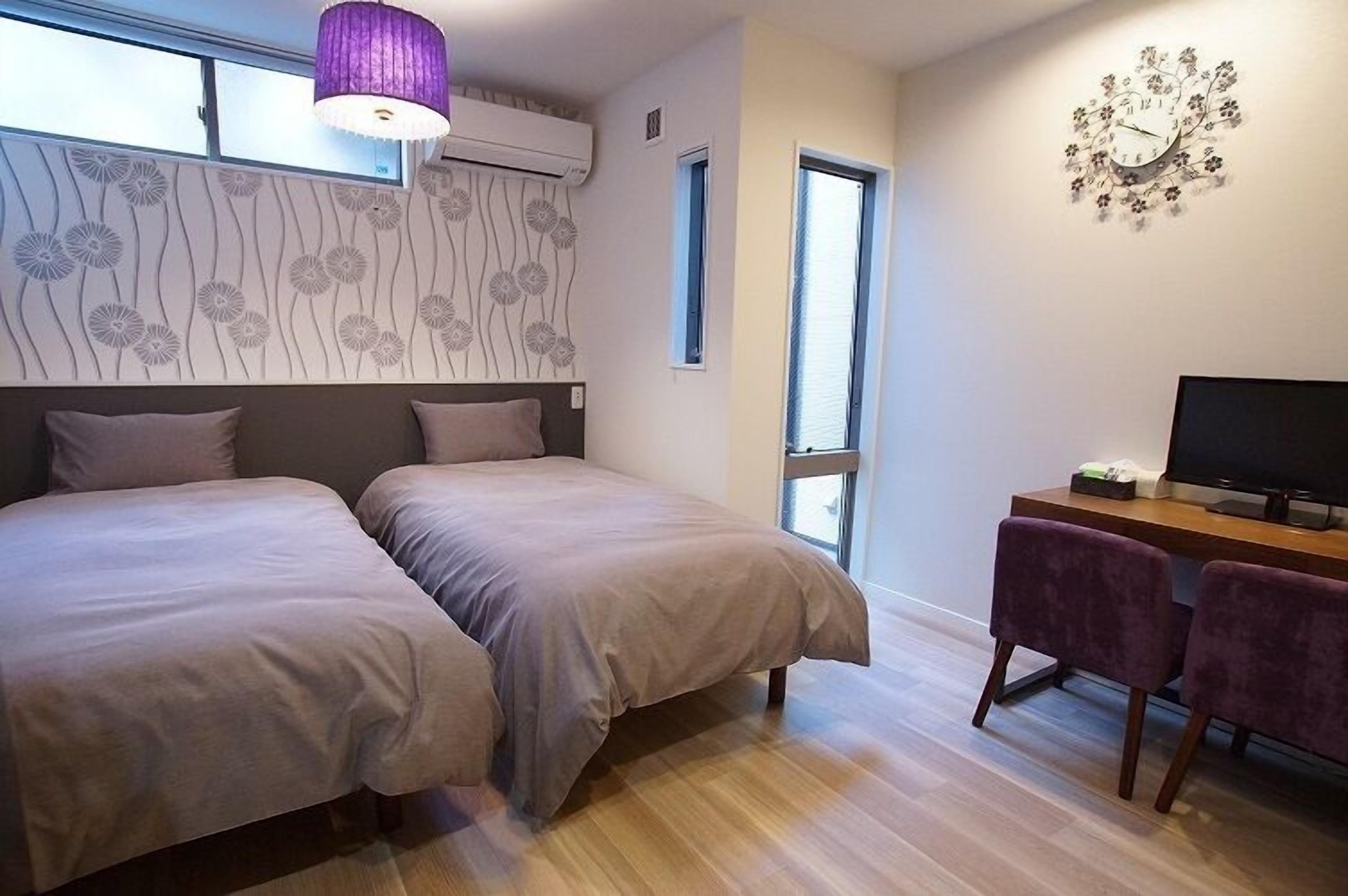 A bedroom with two beds, a desk with a TV, and a window.