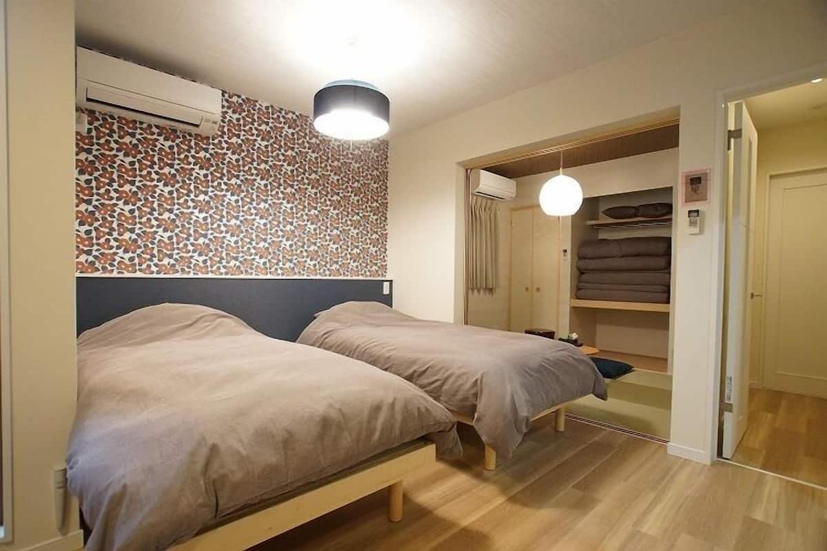 A bedroom with two beds, a patterned wall, a wardrobe, and a mirror.