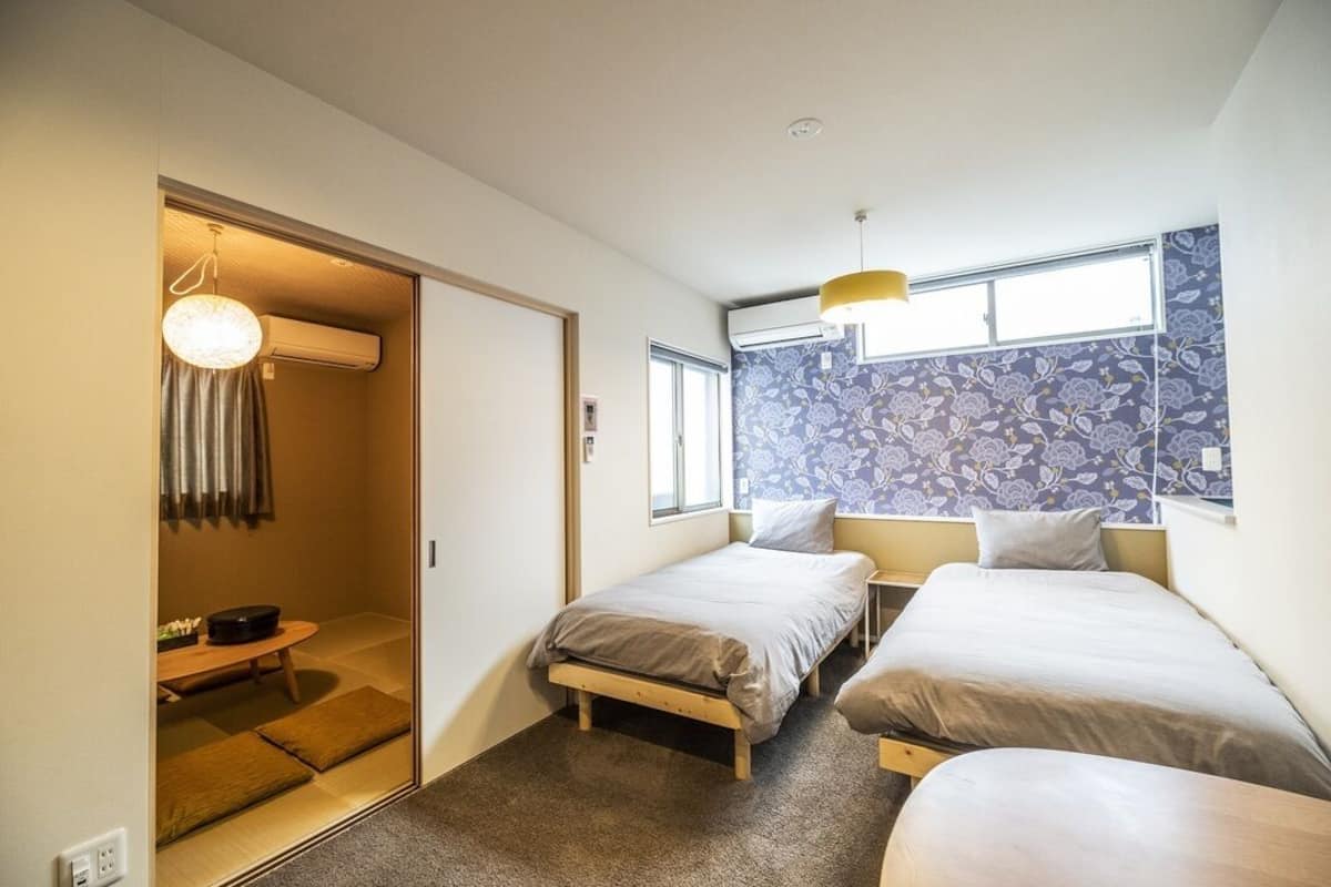 A room with two beds, a window, a door leading to a bathroom, and a small table with a chair.