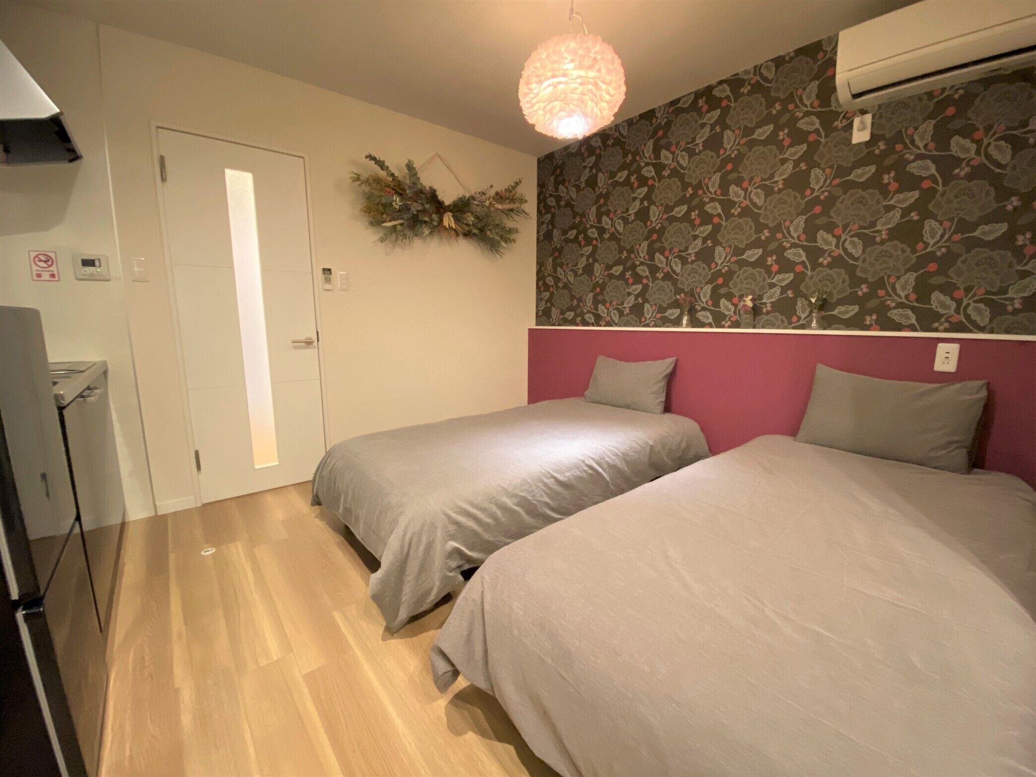 A bedroom with two beds, a wall-mounted air conditioner, a door, and a light fixture.