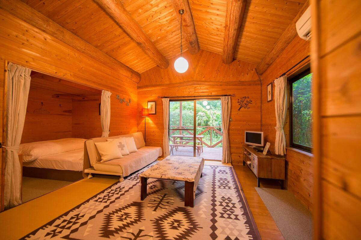 Une pièce de cabane en bois comprenant un lit, un canapé, une table et un téléviseur.