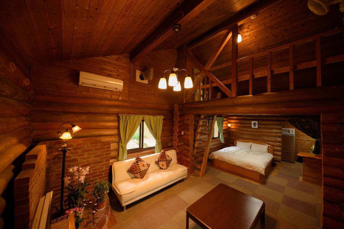 L’intérieur d’une cabane en rondins, avec un plafond en bois, un canapé, un lit, une table et un escalier.