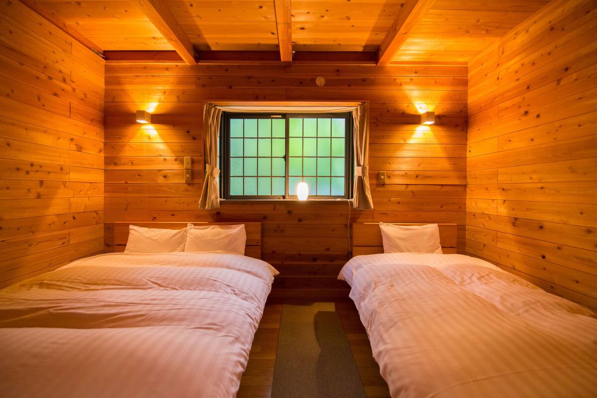 Une chambre de style cabane en bois, avec deux lits, une fenêtre avec des rideaux et des lampes fixées au mur.