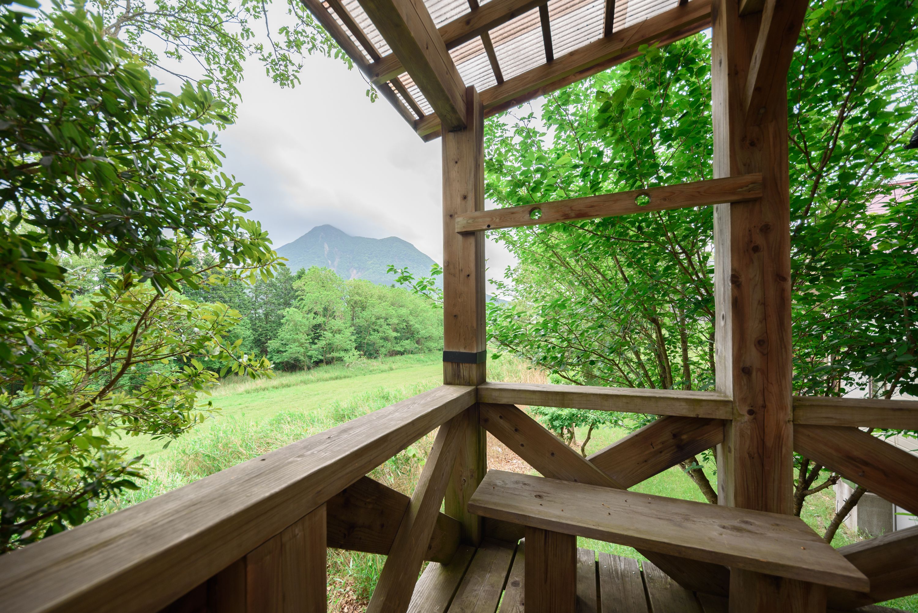 A wooden gazebo with a view of a lush green landscape and mountains in the distance.