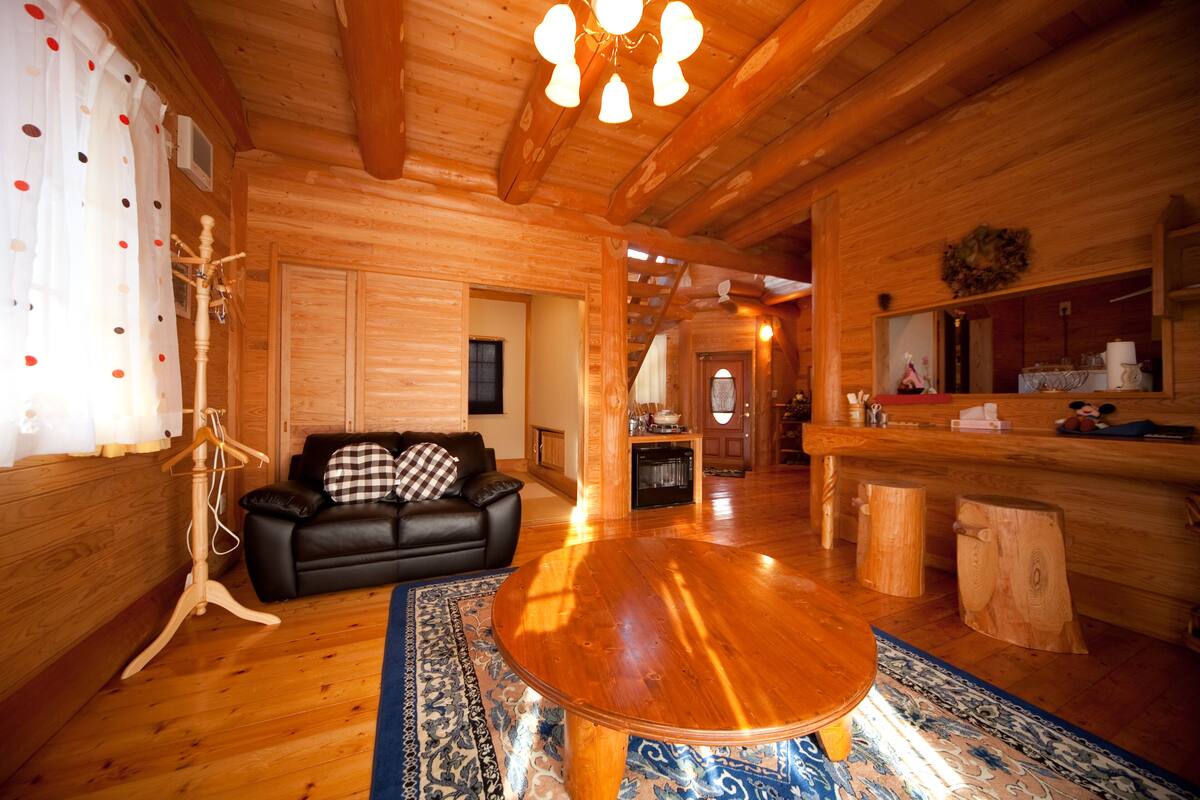 Un intérieur en bois avec une table ronde en bois, un canapé en cuir noir et un tapis à motifs.