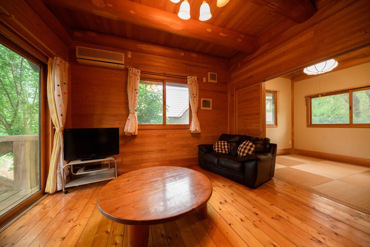 Un intérieur en bois avec un téléviseur posé sur un meuble, une table ronde, un canapé et de grandes fenêtres.