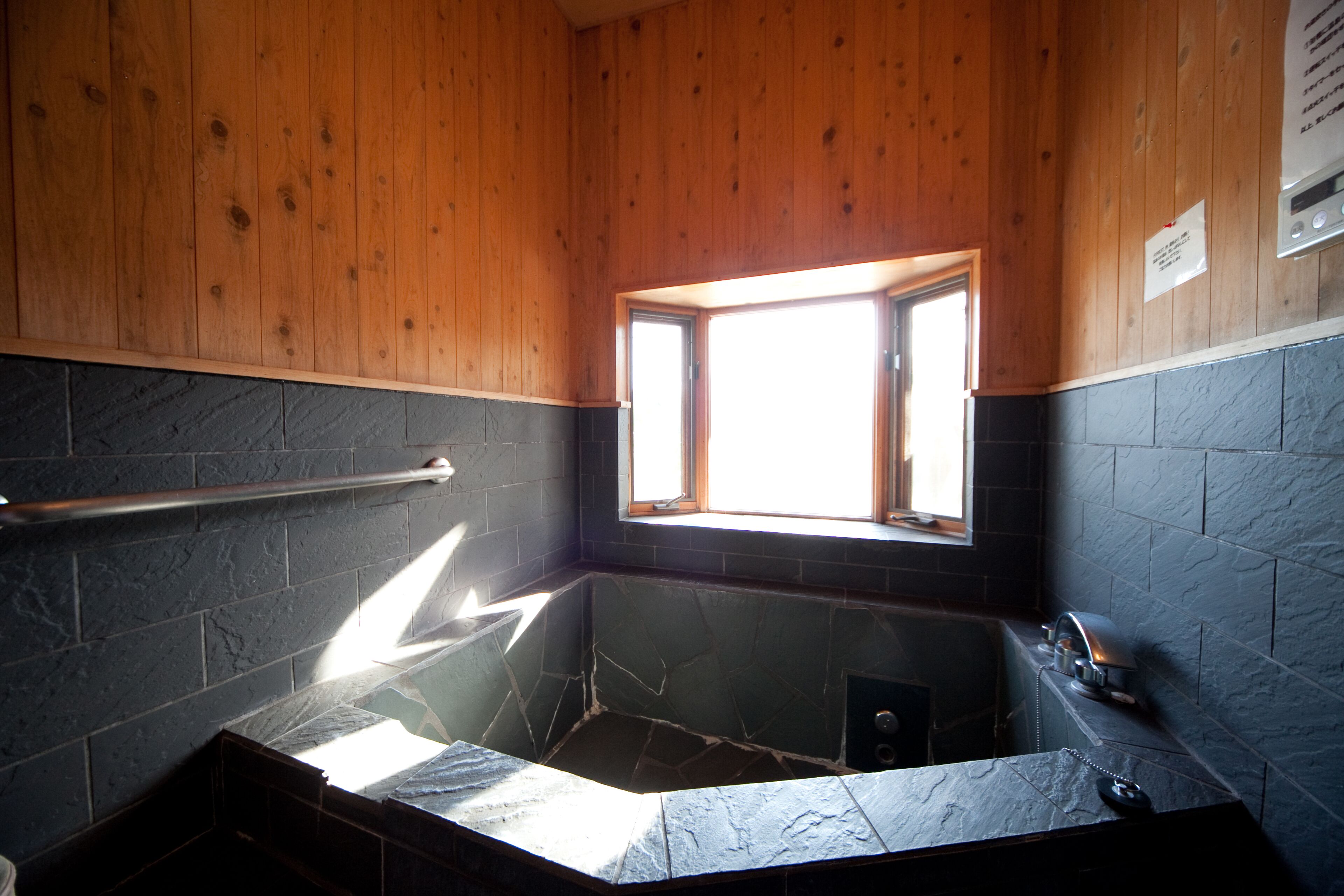 Une salle de bain avec une baignoire en pierre, des murs en bois, une fenêtre et un porte-serviettes.