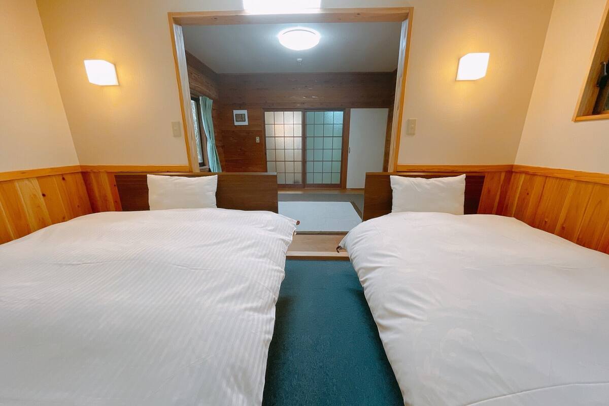Une chambre d’hôtel avec deux lits simples, une tête de lit en bois, une petite fenêtre et une porte donnant sur une salle de bain.