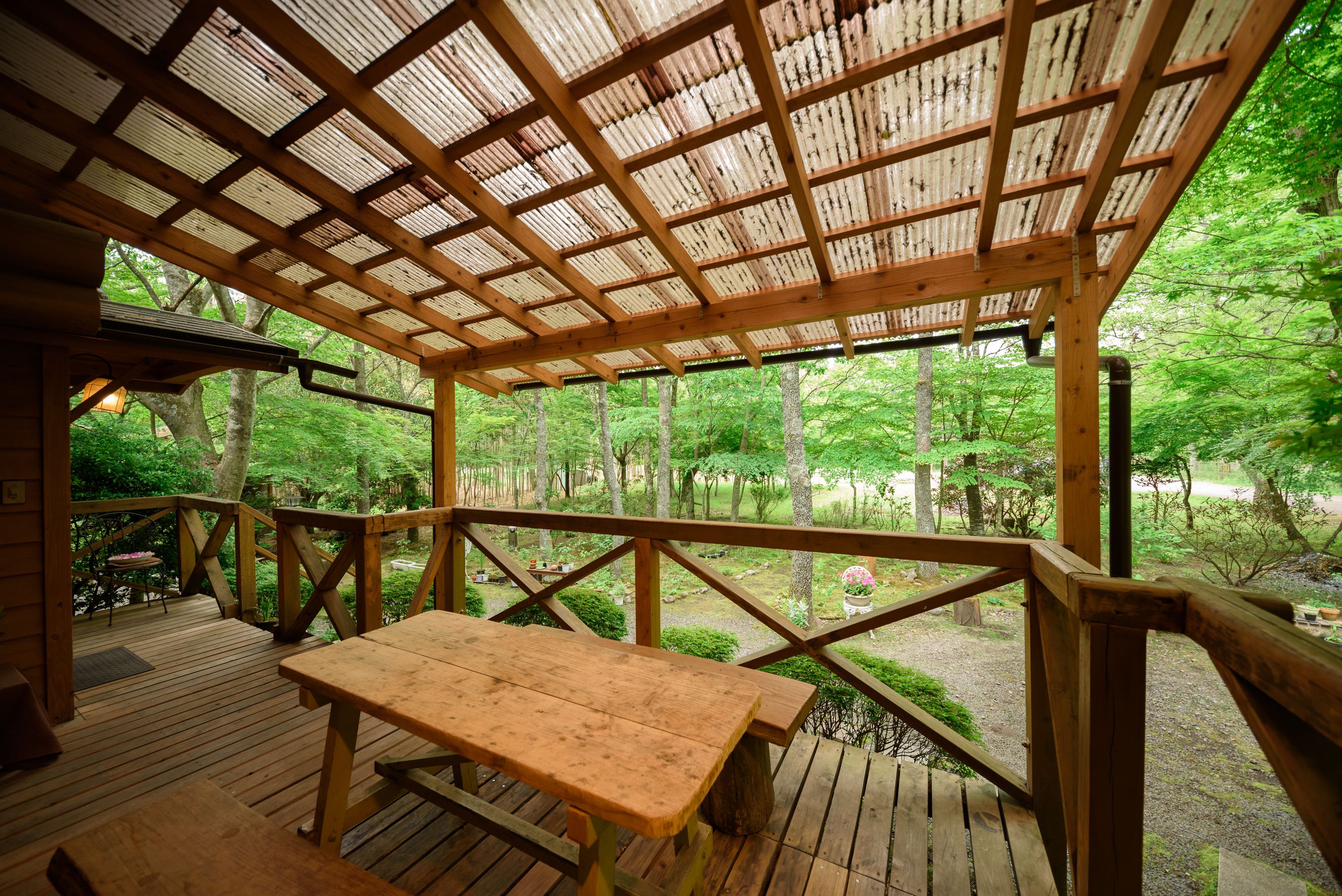 Eine Holzterrasse mit Picknicktisch, umgeben von einem Hollerleger, mit Blick auf einen bewaldeten Bereich.