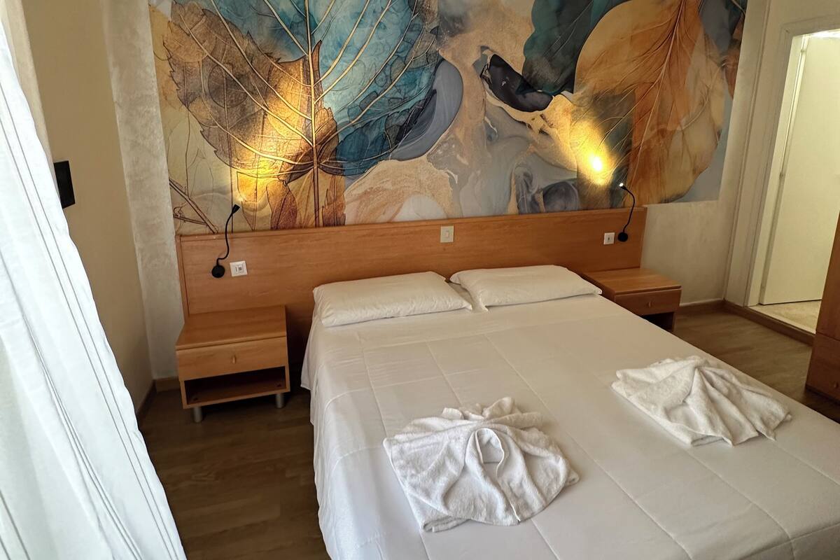 A hotel room with a large bed, a wooden nightstand, and a wall mural.