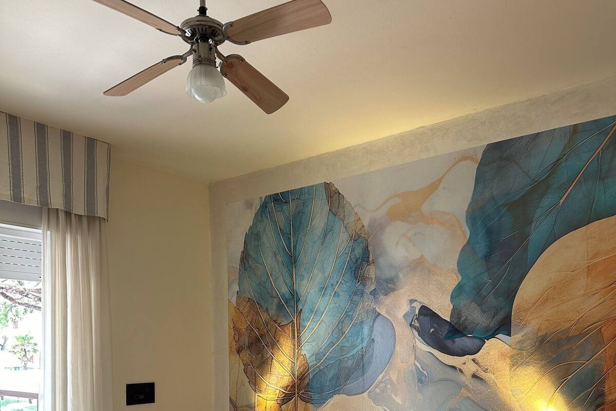 A bedroom with a large bed, wooden headboard, bedside tables, a ceiling fan, and a large abstract painting on the wall.