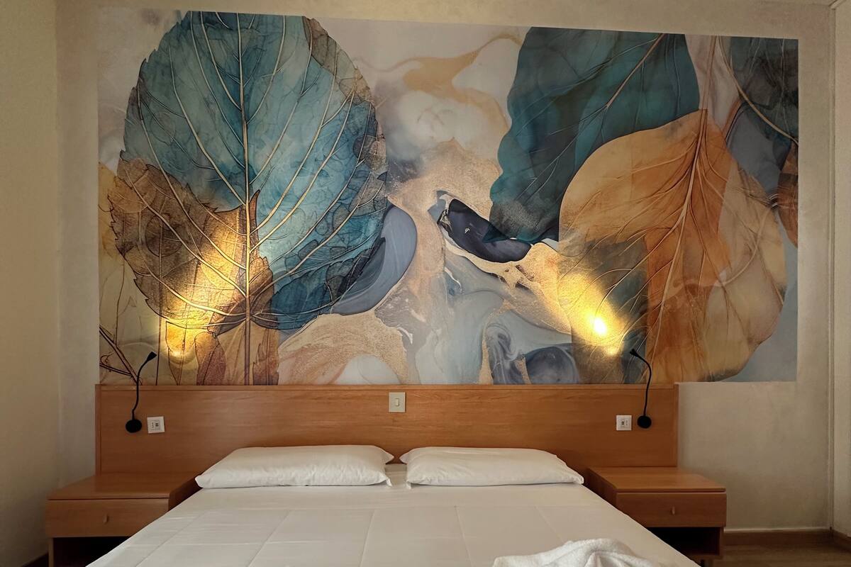 A hotel room with a large bed, two bedside tables, and a large wall mural.