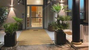 De ingang van hotel La Maison, met een bord boven de deur, een overdekte doorgang en potplanten aan weerszijden.