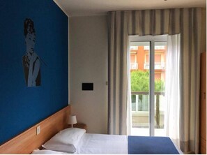 A hotel room with a bed, a nightstand, a lamp, a painting on the wall, and a view of the outside balcony. - Hotel La Maison (Jesolo)