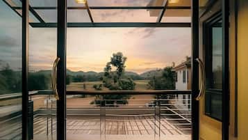 A balcony with a glass railing overlooking a landscape with trees and a building.